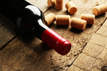 Glass bottle of wine with corks on wooden table background