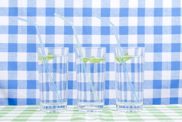 Wall Mural - glass of clean water with mint on a table covered with a checker