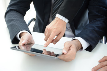 Two businessmen using tablet pc with one hand touching screen