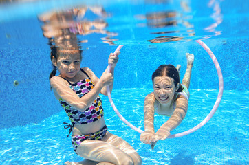 Happy children swim in pool underwater, girls swimming