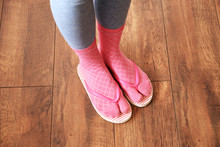 Female Feet In Socks With Pink Flip-flops, On Floor Background