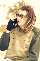 Wall Mural - young rasta guy outdoor talking with smart phone with a warm fil