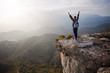 Young woman standing on cliff with outstretched arms