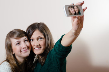 2 young attractive adorable women happy smiling & looking at camera having fun friendly hugging and making selfie on light copy space background portrait picture