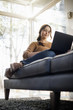 © Mint Images - Low angle view of a woman sitting on a sofa looking at her laptop.