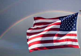 American flag against a cloudy sky with a rainbow