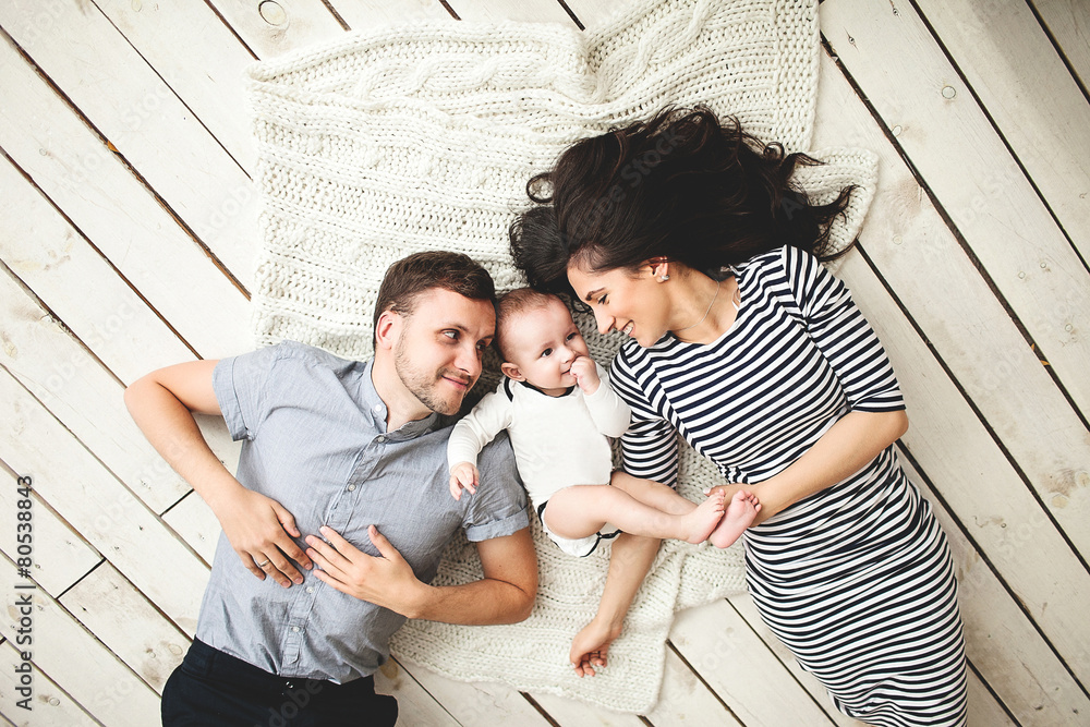 Young father, mother and cute baby lying on floor - obrazy, fototapety, plakaty 