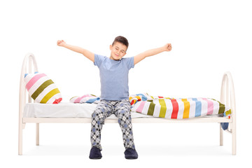 Fototapete - Little boy stretching seated on a bed