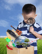 Boy using magnifying glass with toys and globe burst from wooden