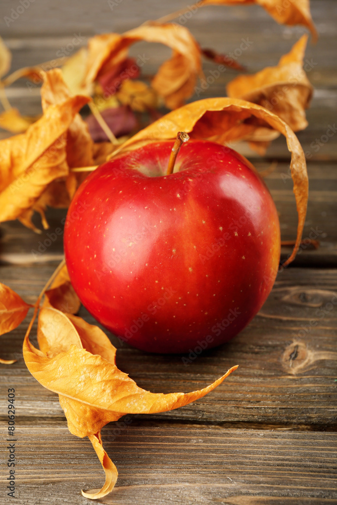 Apple with dried leaves on wooden table, closeup