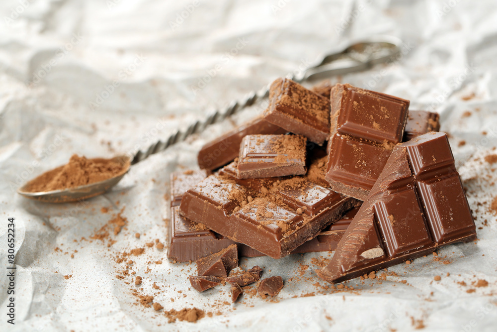 Pieces of chocolate with cocoa on parchment, closeup