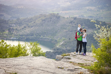Wall Mural - Young couple with toddler boy standing on cliff and kissing