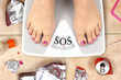 © viperagp - Feet on bathroom scale with word SOS and junk food garbage