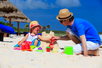 Wall Mural - father and little daughter building sandcastle on the beach