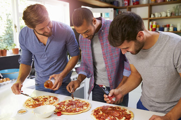 Three Male Friends Making Pizza In Kitchen Together