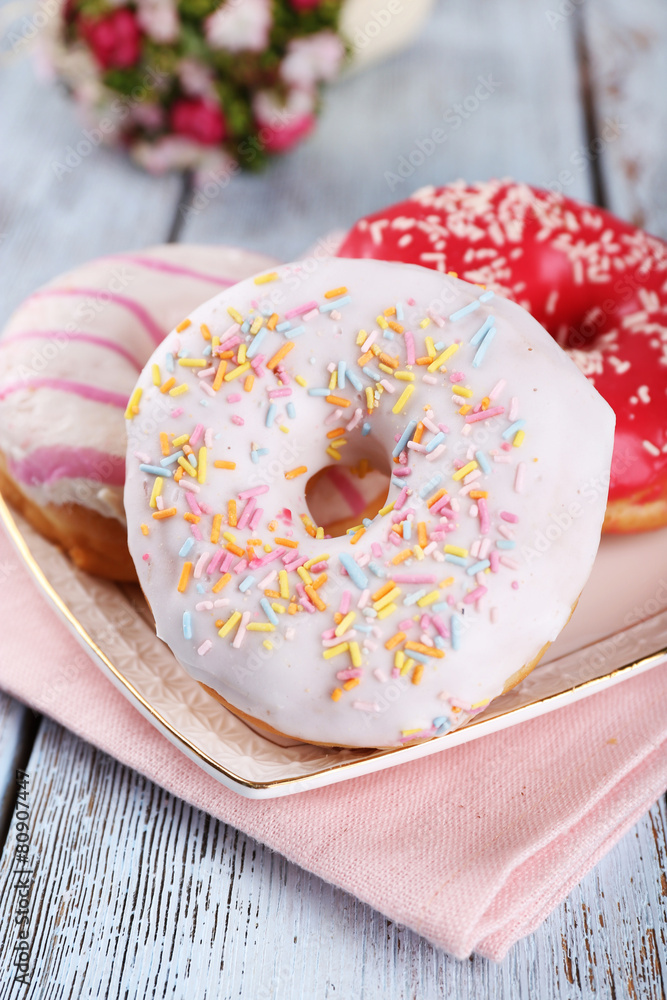 Delicious donuts with icing on plate on wooden background