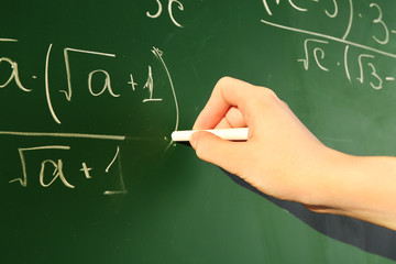 Teacher hand writing formulas on blackboard background