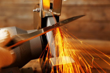 Knife sharpener and hand with blade on wooden table, closeup