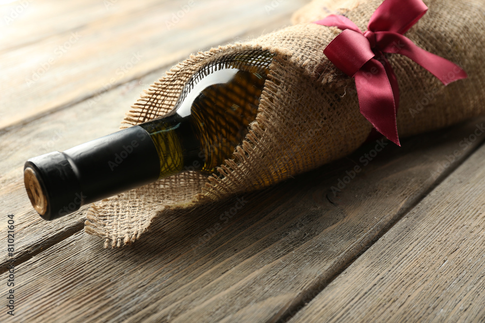 Wine bottle wrapped in burlap cloth on wooden planks background