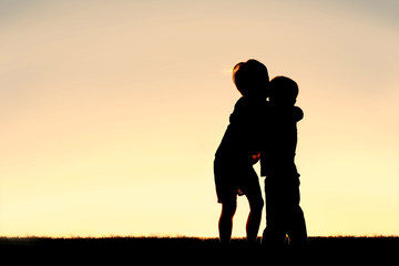 silhouette of two young children hugging at sunset