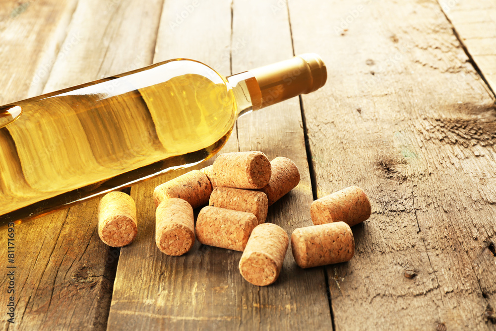 Glass bottle of wine with corks on wooden table background