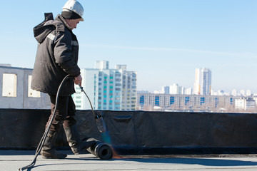 Roofer man worker installing roll of roofing felt