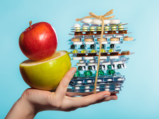 Human hand holding stack of pills and fruits on blue.