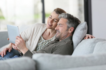 Mature couple using digital tablet relaxing in sofa