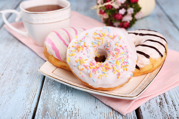 Canvas Print - Delicious donuts with icing on plate on wooden background