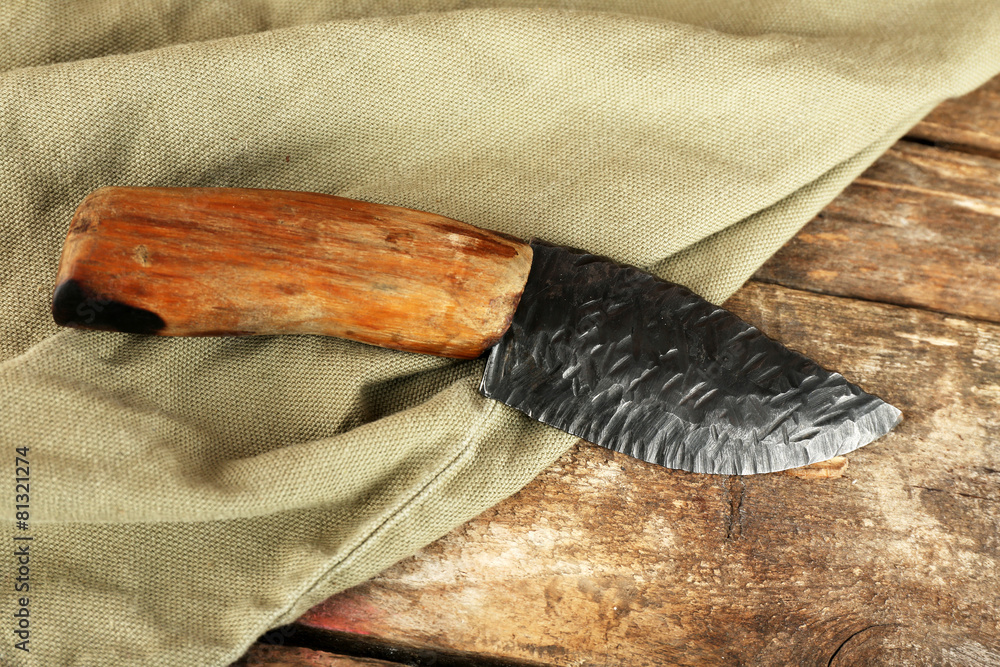 Hunting knife on wooden table with sackcloth, closeup