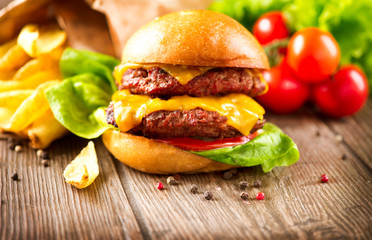 Cheeseburger with fresh salad and french fries on a wooden table