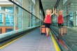 © Tropical studio - Joyful girl with her trunk on airport moving walkway