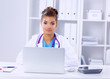 © lenets_tan - Female doctor sitting on the desk and working a laptop in
