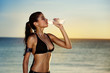 © luckybusiness - Fitness woman drinking water after exercising on summer day in b