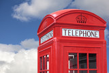Fototapeta Londyn - London red telephone box booth isolated against a fluffy clouds blue sky photo