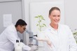 © WavebreakmediaMicro - Happy scientist smiling at camera showing plant