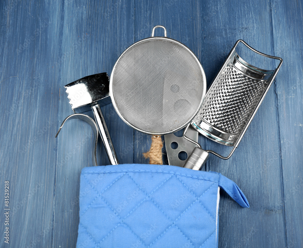 Different kitchen utensils in potholder on wooden background