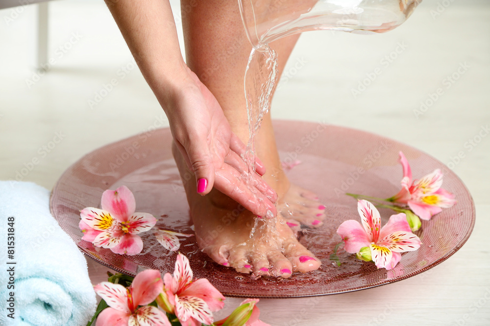 Woman washing beautiful legs in bowl, on light background. Spa procedure concept
