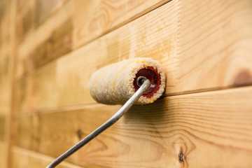 Painter covers wooden wall with a protective varnish