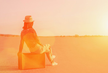 Poster - Traveler woman sitting on suitcase on road at sunny day