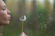 Young woman in the park holding blowing dandelion flower seed