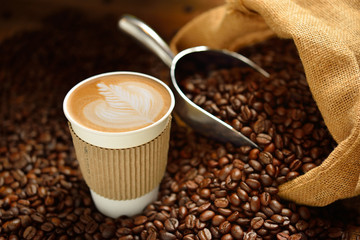 Paper cup of coffee latte and coffee beans on wooden table