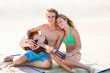 © lunamarina - Blond tourist couple playing guitar at beach
