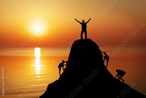 Fotomural Silhouette of a mans on a mountain top on sunset background.