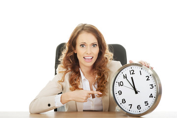 Businesswoman with clock by a desk.