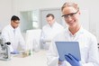 © WavebreakMediaMicro - Smiling scientist using tablet while colleagues working behind