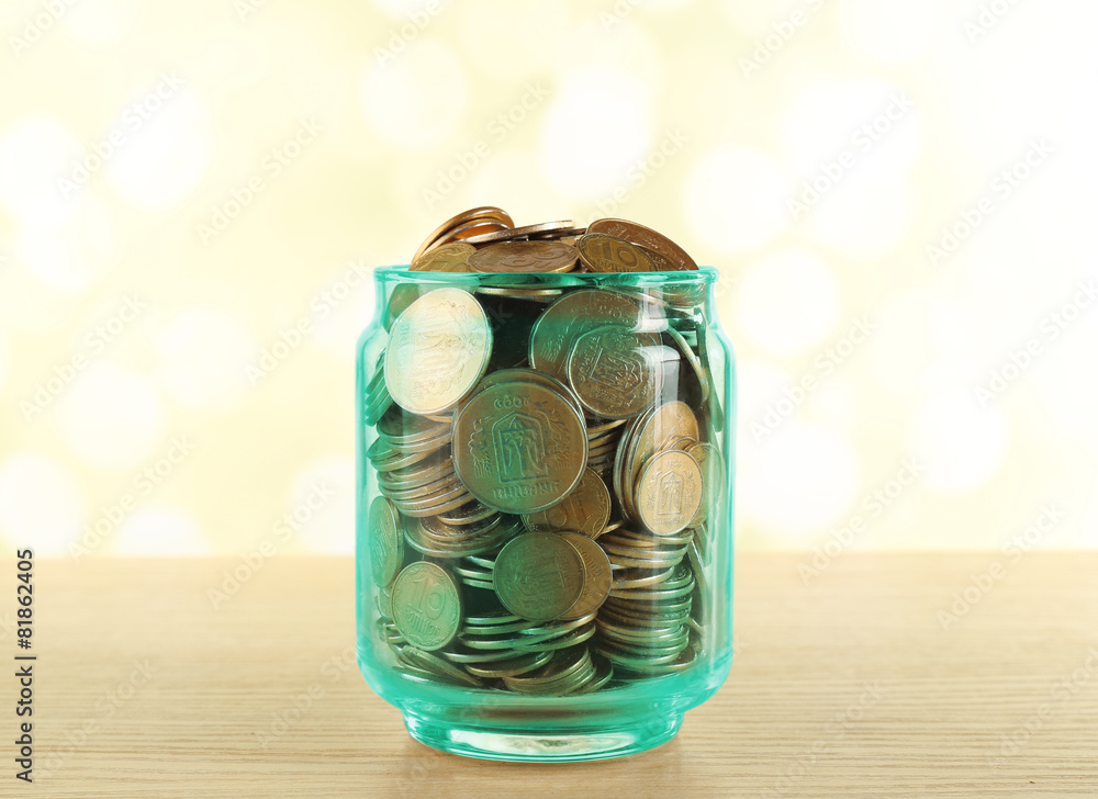 Gold coins in glass bottle on bright blurred background