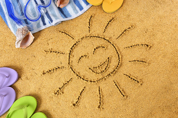 Smiling sun happy smiley face drawing drawn in sand with child hands on a tropical beach with seashells and accessories summer holiday vacation photo