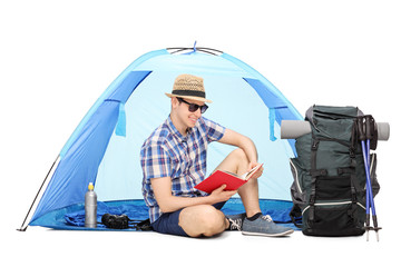 Wall Mural - Young camper reading a book seated on the ground