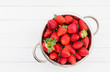 Fresh strawberries in rustic colander on white wooden table